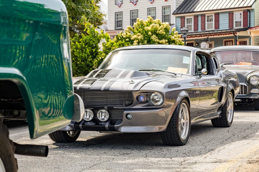 Silver fastback Mustang with black racing stripes on a tree-lined main street