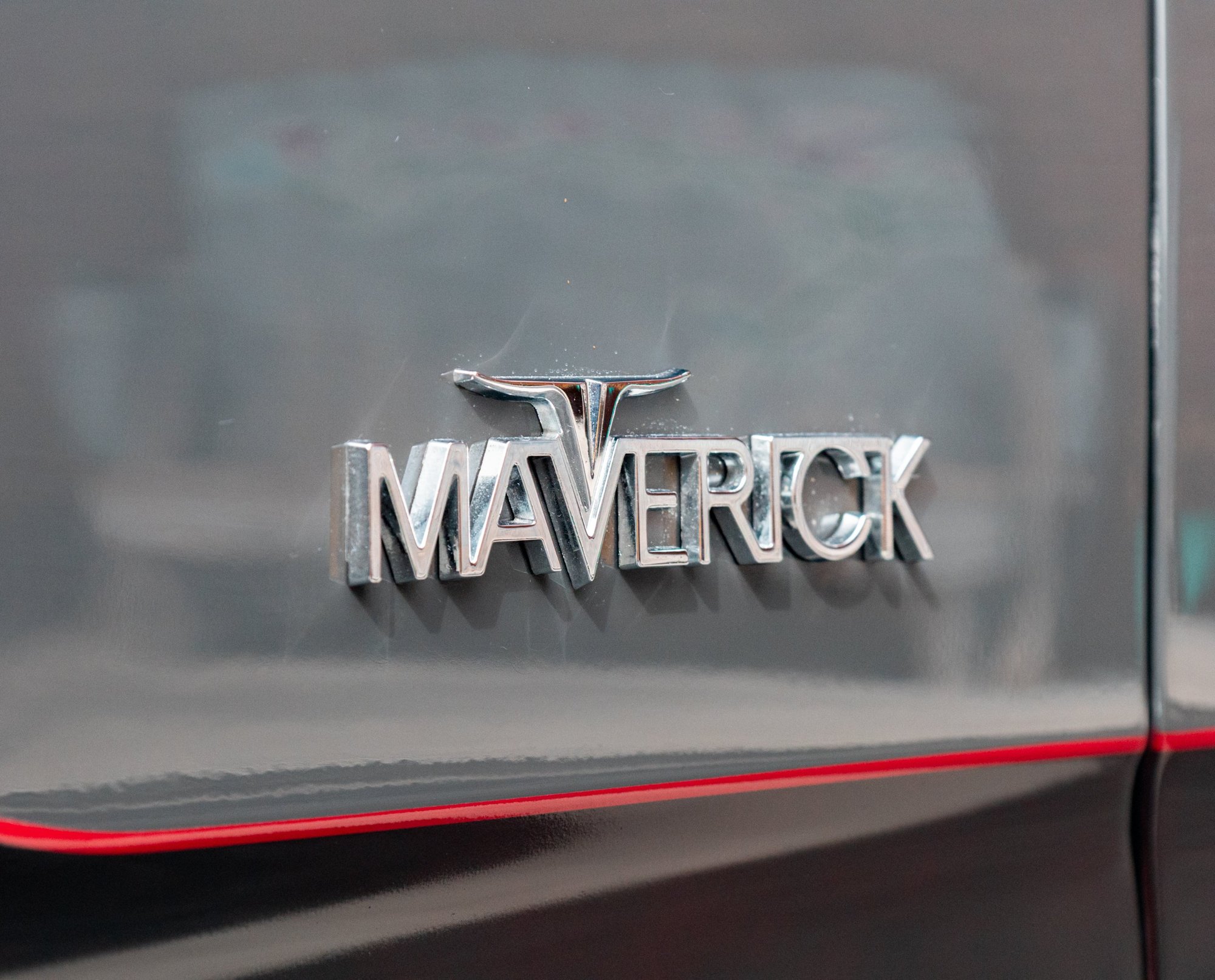 Chrome Maverick script badge on grey paint above a red pinstripe