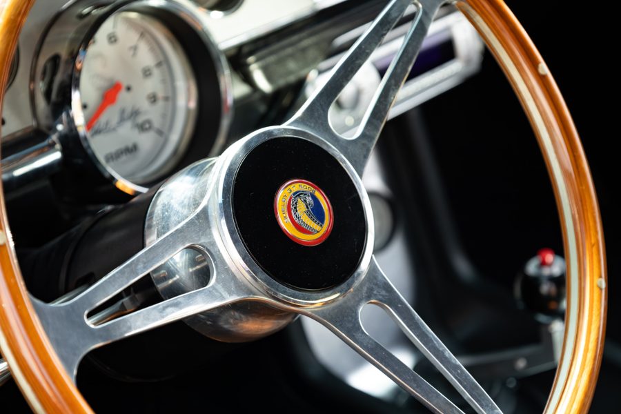 Polished three-spoke steering wheel with a wood rim and Shelby horn badge, tachometer behind
