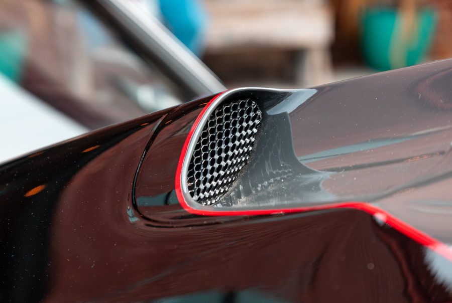 Close-up of a gloss black hood scoop with a honeycomb grille and red pinstripe