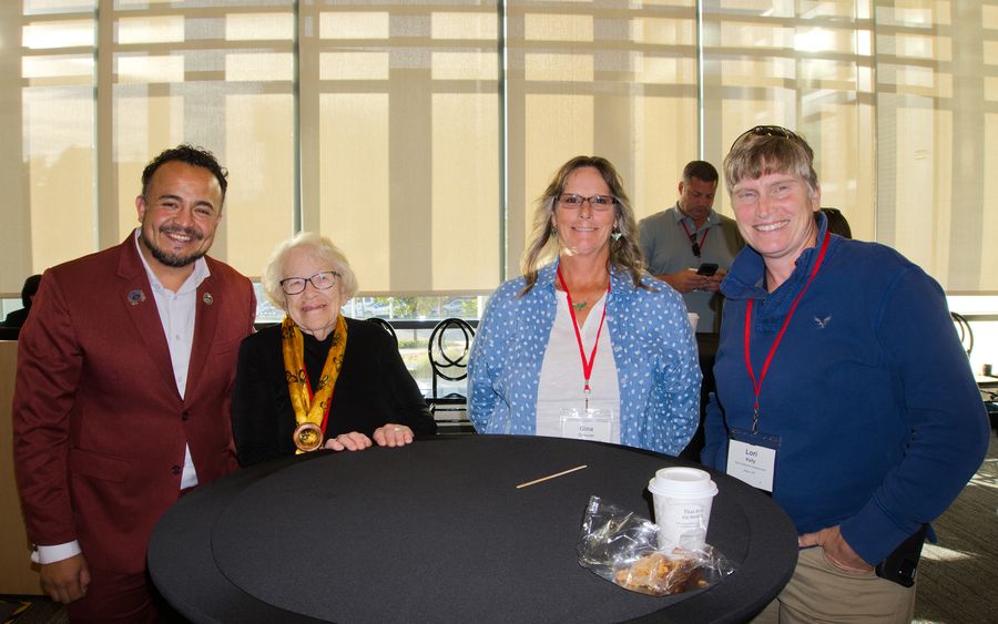 Four guests posing together at a cocktail table in a sunlit hall