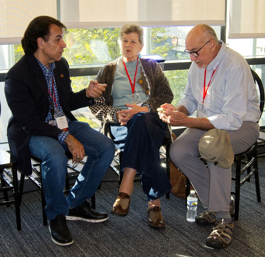 Three people in animated conversation, seated by a bright window