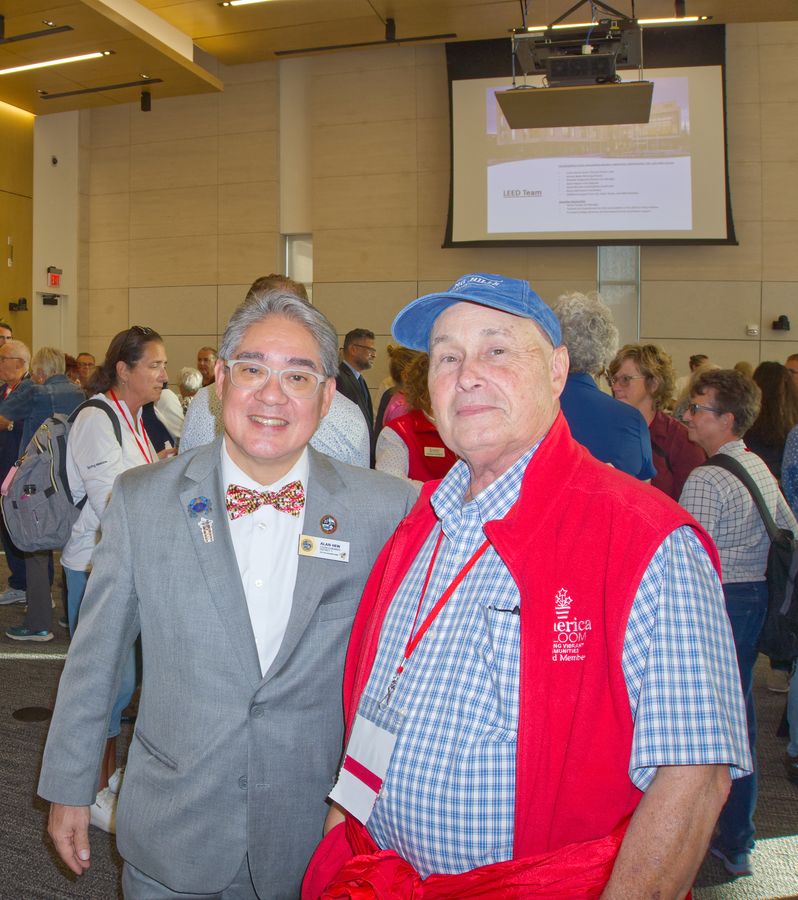 Two smiling men, one in a bow tie and one in a red volunteer vest