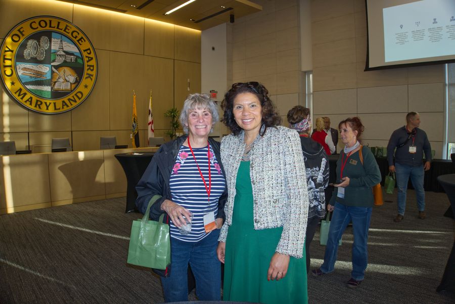 Two women posing in front of the City of College Park seal