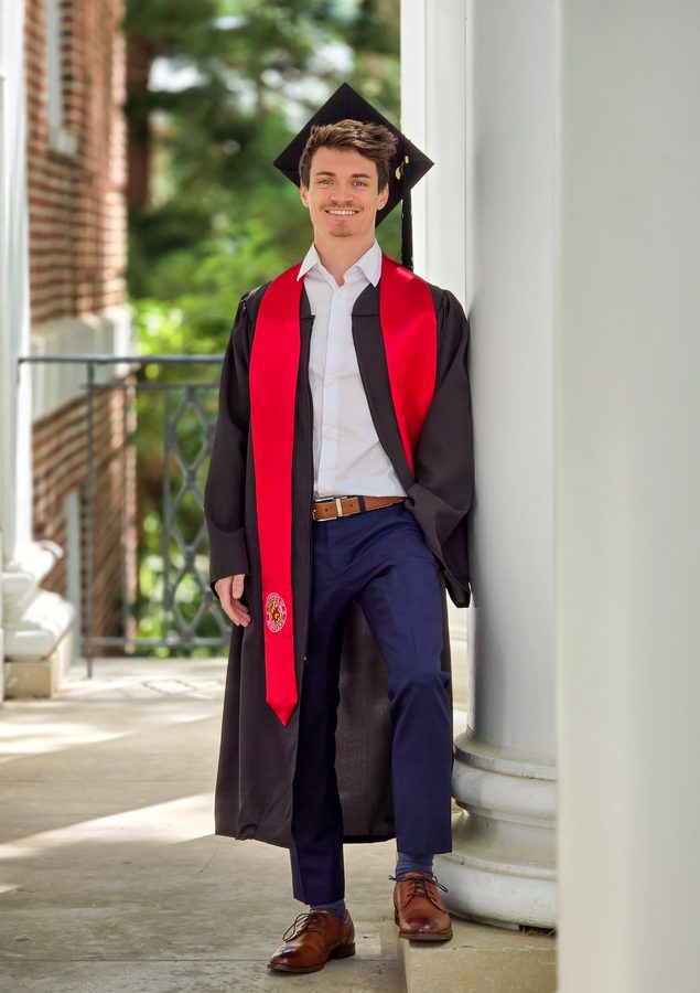 Graduate leaning against a white column in cap and gown