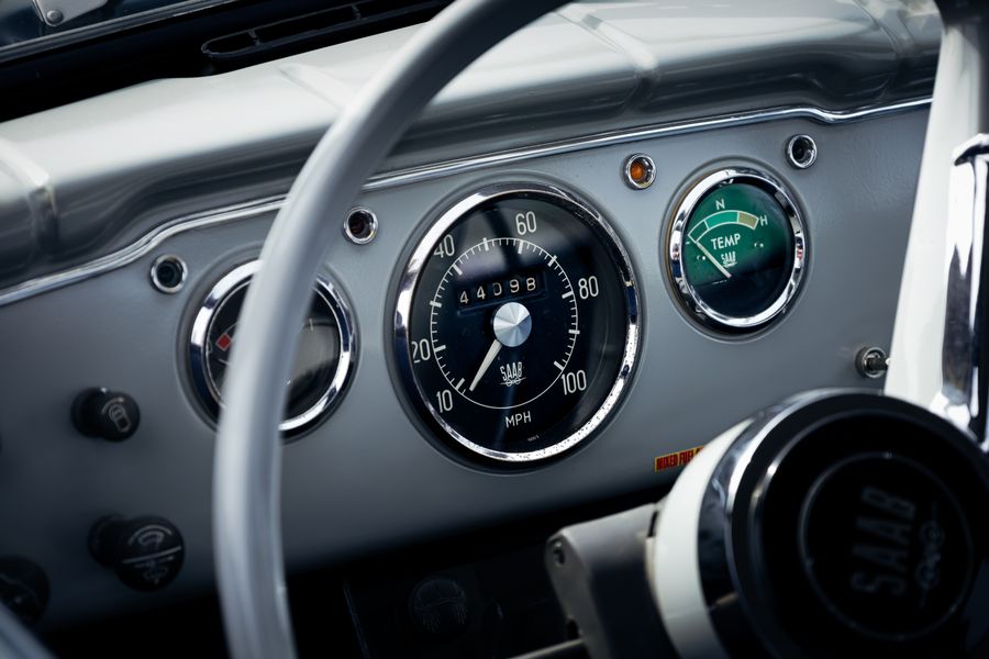 Cream steering wheel in front of chrome-ringed speedometer and temperature gauges on a classic Saab dash