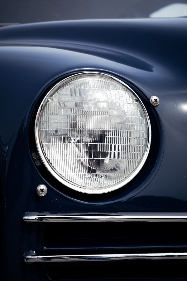 Round headlight and chrome trim strips on a navy classic Saab