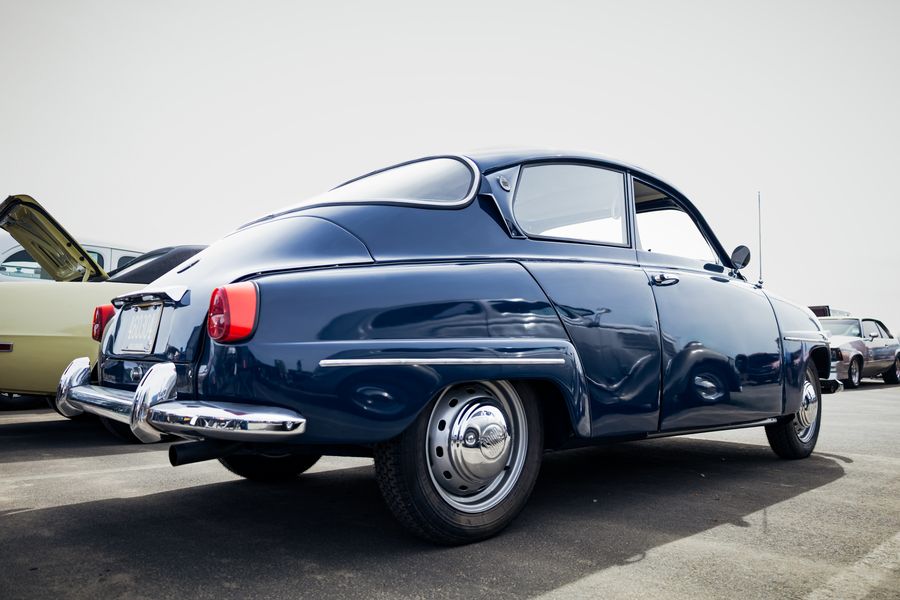 Rear three-quarter view of a navy classic Saab with its fastback roofline at a car show